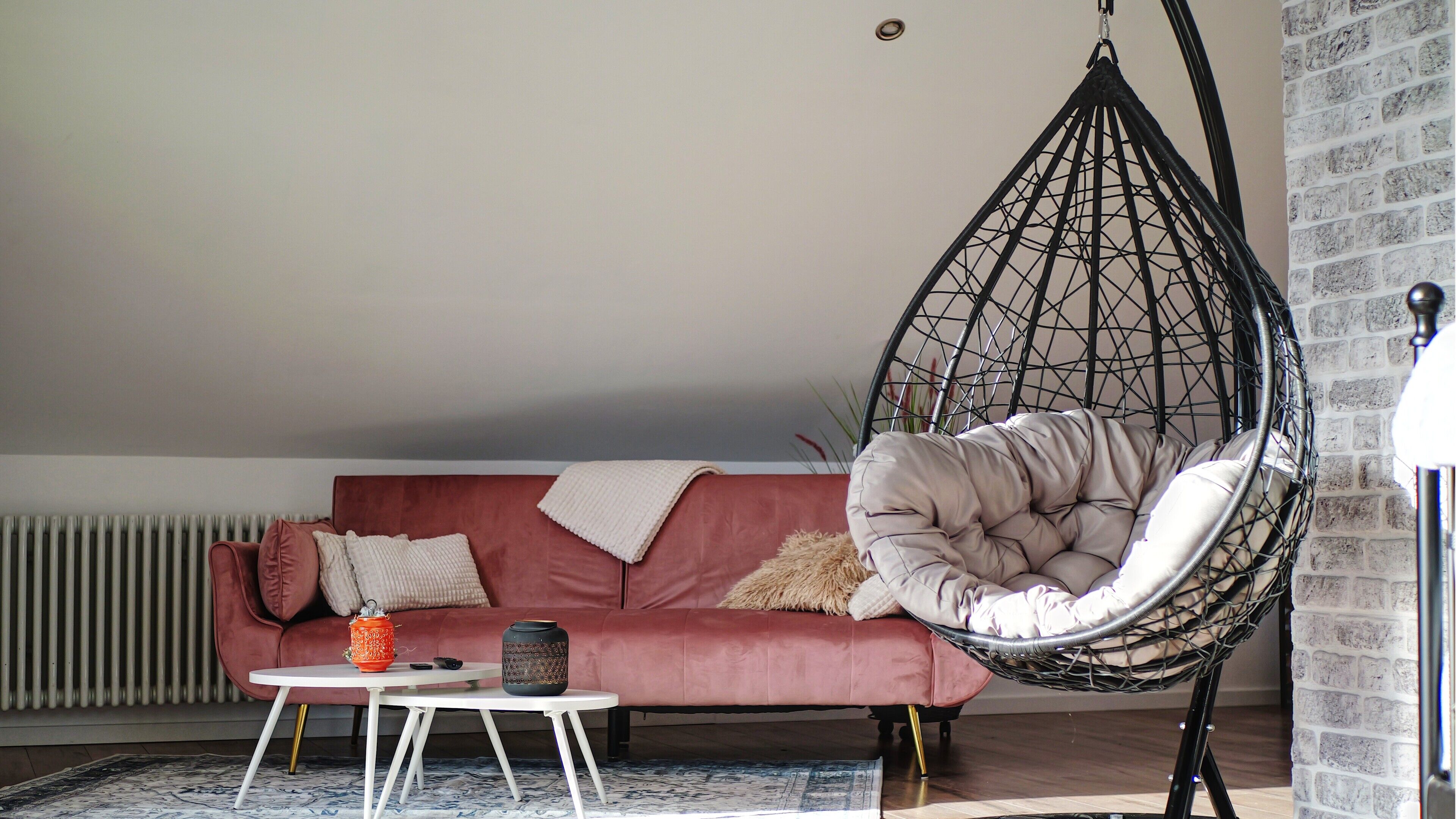 Een kamer met een hangstoel, een bank, een bijzettafeltje en een radiator.