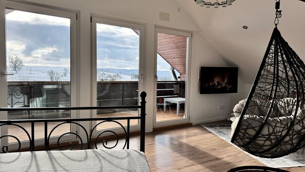 Ett sovrum med ett stort fönster, en hängstol, en tv och utsikt över ett snötäckt landskap.