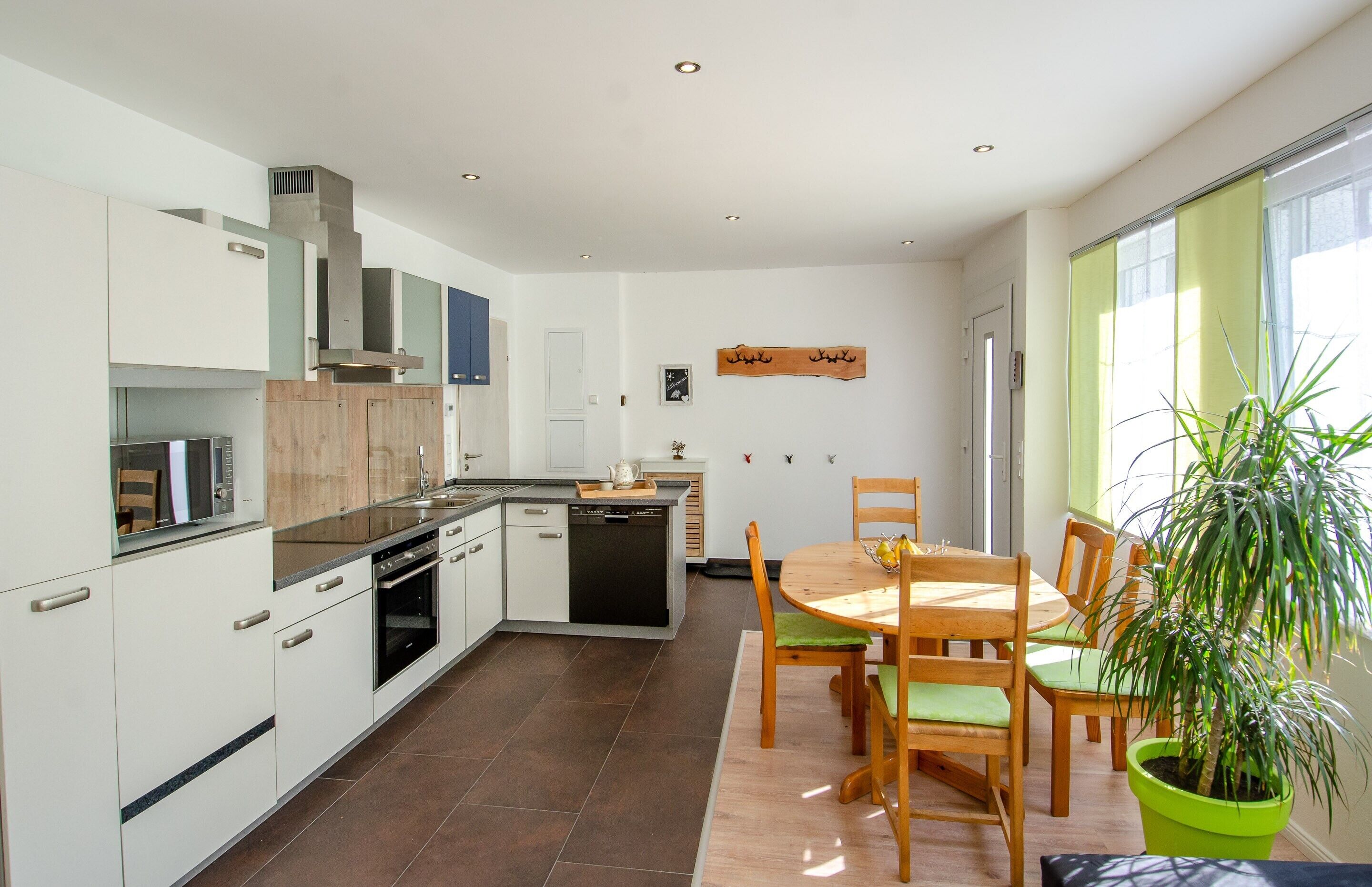 Eine moderne Küche mit weißen Schränken, eine Essecke mit einem Holztisch und Stühlen sowie ein großes Fenster mit Blick.