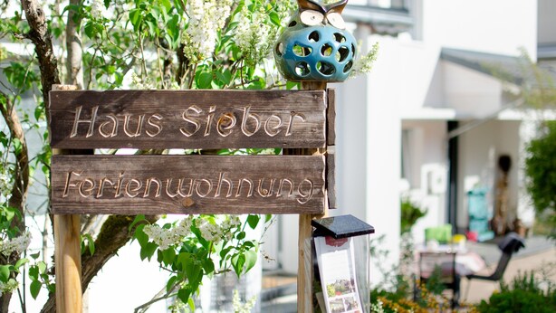 Une pancarte en bois indiquant « Haus Sieber Ferienwohnung », ce qui signifie qu’il s’agit d’une maison de vacances à louer.