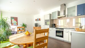 Une cuisine moderne avec des meubles blancs, une table à manger en bois avec des coussins verts et une machine à café.
