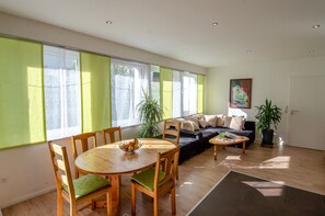 Ein modernes Wohnzimmer mit Esstisch, Sofa und großen Fenstern.