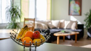 Un panier de fruits est posé sur une table dans un salon, où se trouvent un canapé et un tableau accroché au mur.