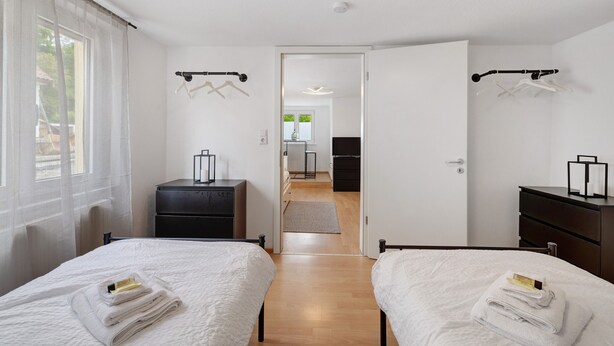 Une chambre d’hôtel avec deux lits, un bureau, une armoire et une salle de bain visible à travers une porte ouverte.