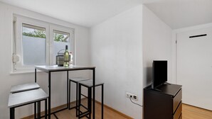 Une pièce avec une fenêtre, un bureau, une chaise, une télévision et une commode.