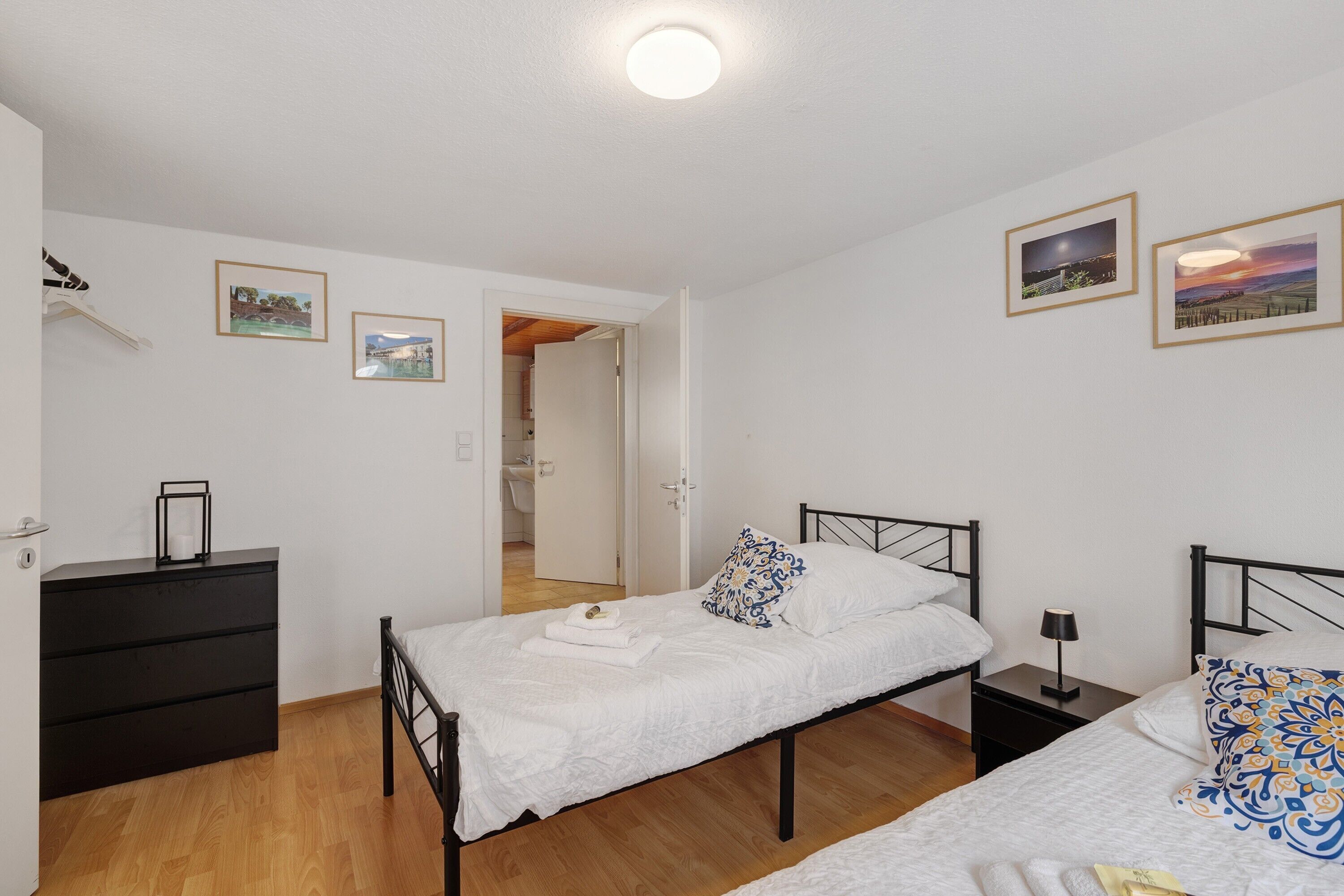 A bedroom with two beds, a dresser, and a nightstand. There are framed pictures on the wall.