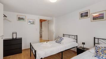 A bedroom with two beds, a dresser, and a nightstand. There are framed pictures on the wall.