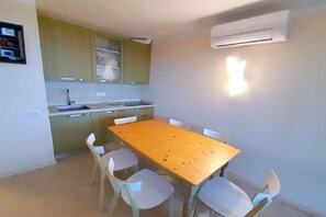 A small kitchen with a dining table and chairs, an air conditioner, and a wall-mounted light fixture.
