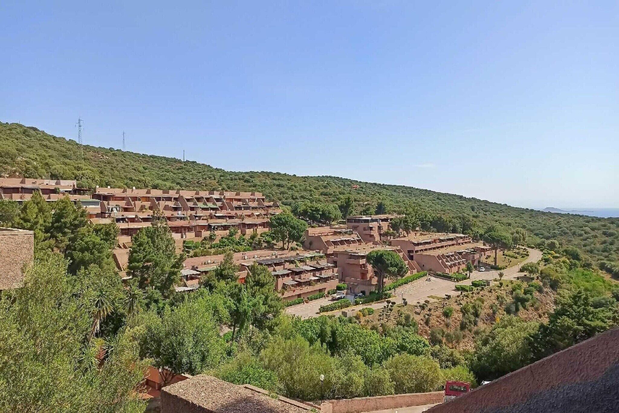 A hillside residential area with terraced houses, surrounded by greenery and a clear sky.