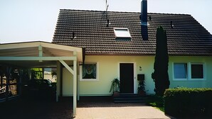 A two-story house with a covered driveway, a chimney, and a small window on the roof.