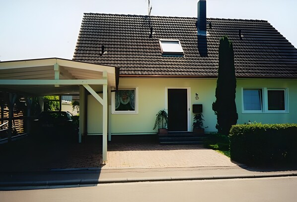 Een huis met twee verdiepingen, een overdekte oprit, een schoorsteen en een klein dakraam.