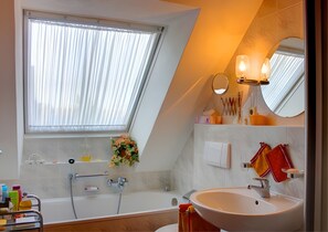 Een moderne badkamer met dakraam, bad, wastafel en spiegel.