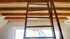 A loft-style room with a wooden ladder, a window with blinds, and a blue chair.