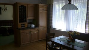 Una cocina con armarios de madera, una mesa de comedor, sillas y un ventanal con cortinas.