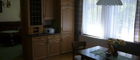 Una cocina con armarios de madera, una mesa de comedor, sillas y un ventanal con cortinas.