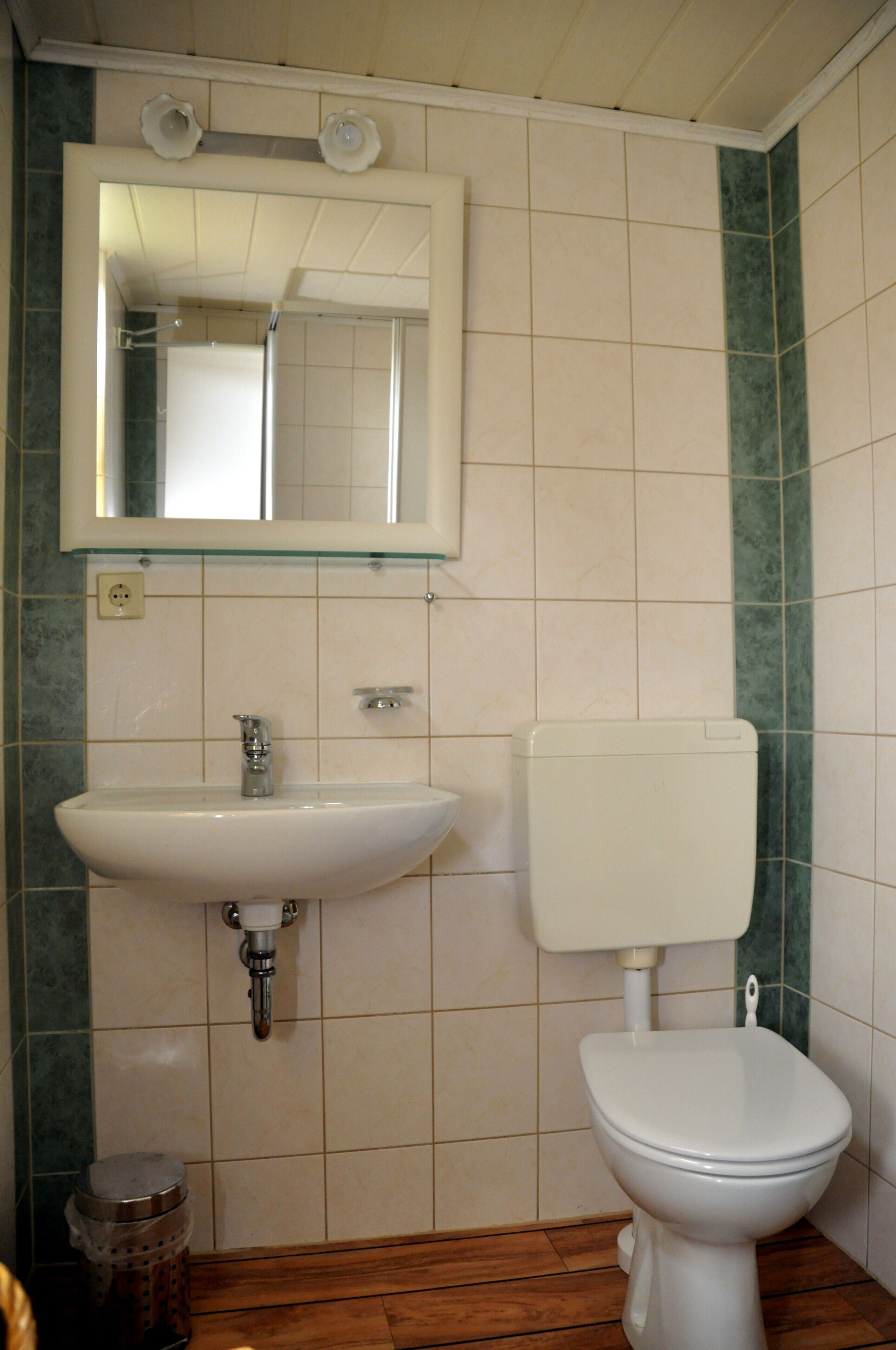 Kylpyhuone, jossa on pesuallas, wc, peili ja laatoitetut seinät.