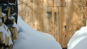 Una puerta de madera con un picaporte metálico y un pequeño ventanal, rodeada de nieve.