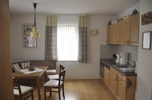 Una cucina compatta con zona pranzo, mobili in legno, un lavandino e una finestra con tende.