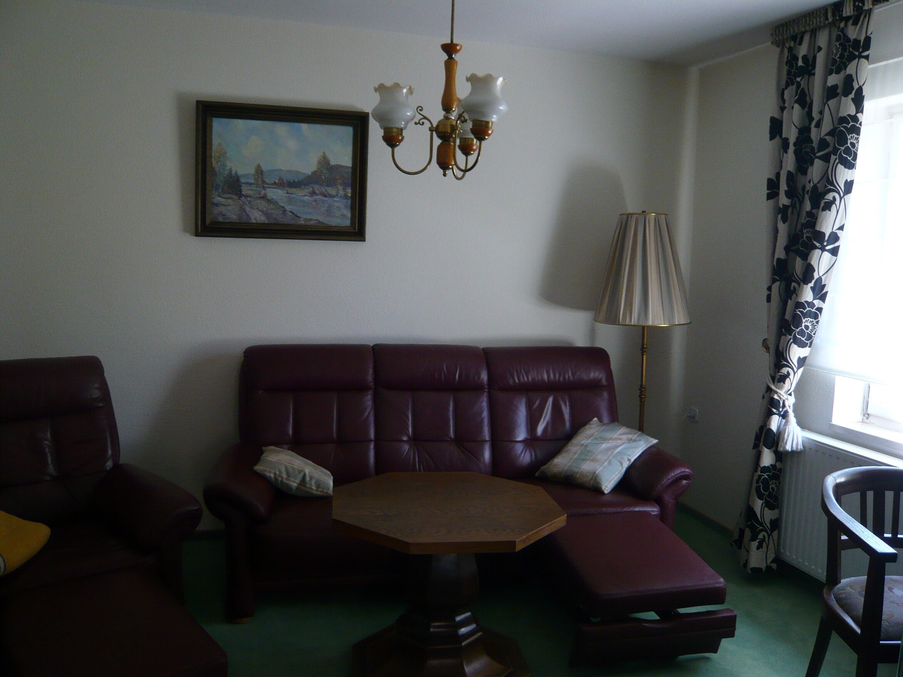 Una habitación con un sofá, una mesita, una lámpara, una silla y un cuadro en la pared.