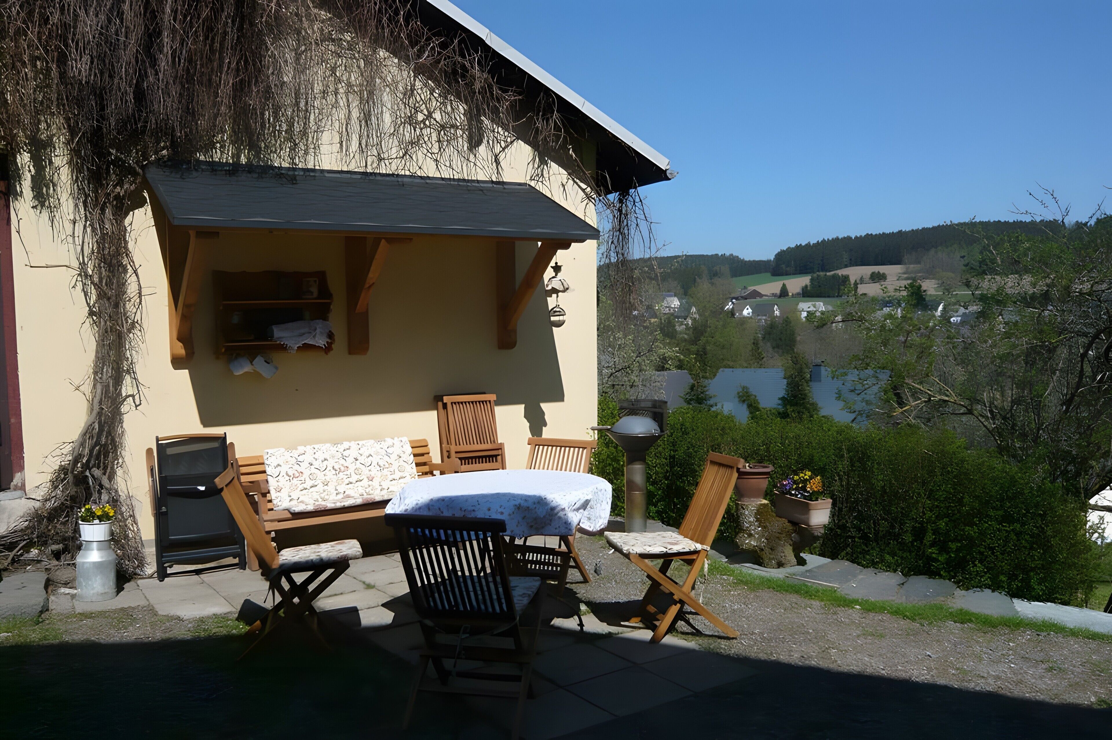 Eine Terrasse mit Tisch, Stühlen, einem Grill und Blick auf ein Dorf.