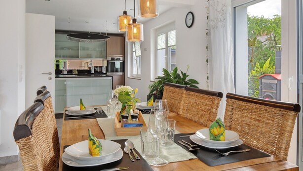 Uma sala de jantar com cadeiras de vime, uma mesa de madeira e luminárias pendentes.