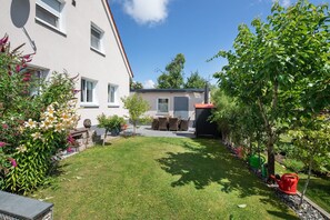 Il s’agit d’une propriété résidentielle dotée d’une pelouse bien entretenue, d’une terrasse avec mobilier d’extérieur et d’un petit jardin agrémenté de diverses plantes et fleurs.