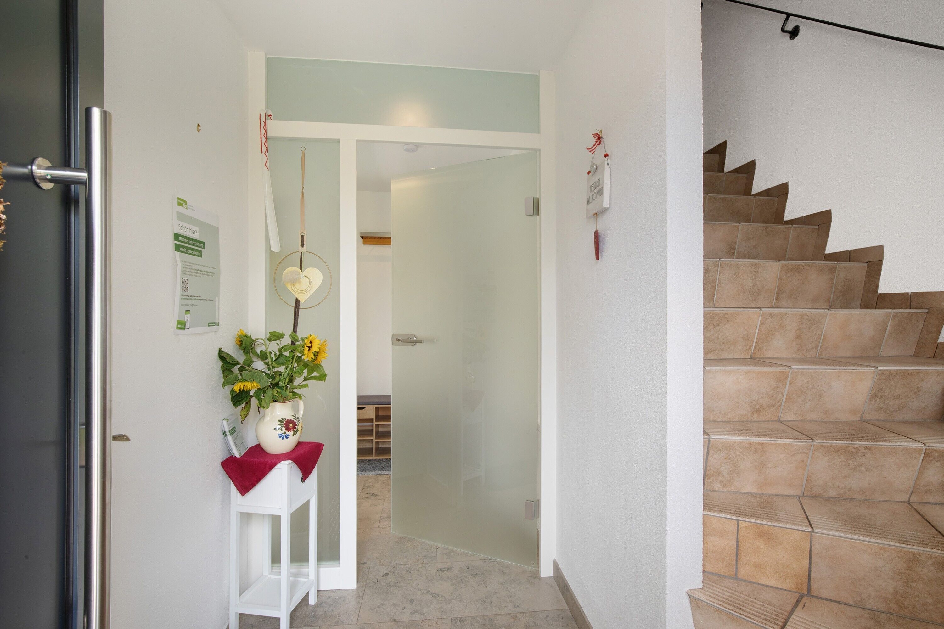A hallway with a white door, a white table with a vase of flowers, and a staircase with beige tiles.