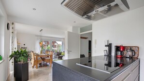 Cozinha moderna com ilha central, área de refeições com mesa e cadeiras, e vista para uma varanda através de uma porta aberta.