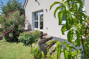 Une maison avec un escalier en pierre menant à une porte en verre, entourée de verdure et sous un ciel dégagé.