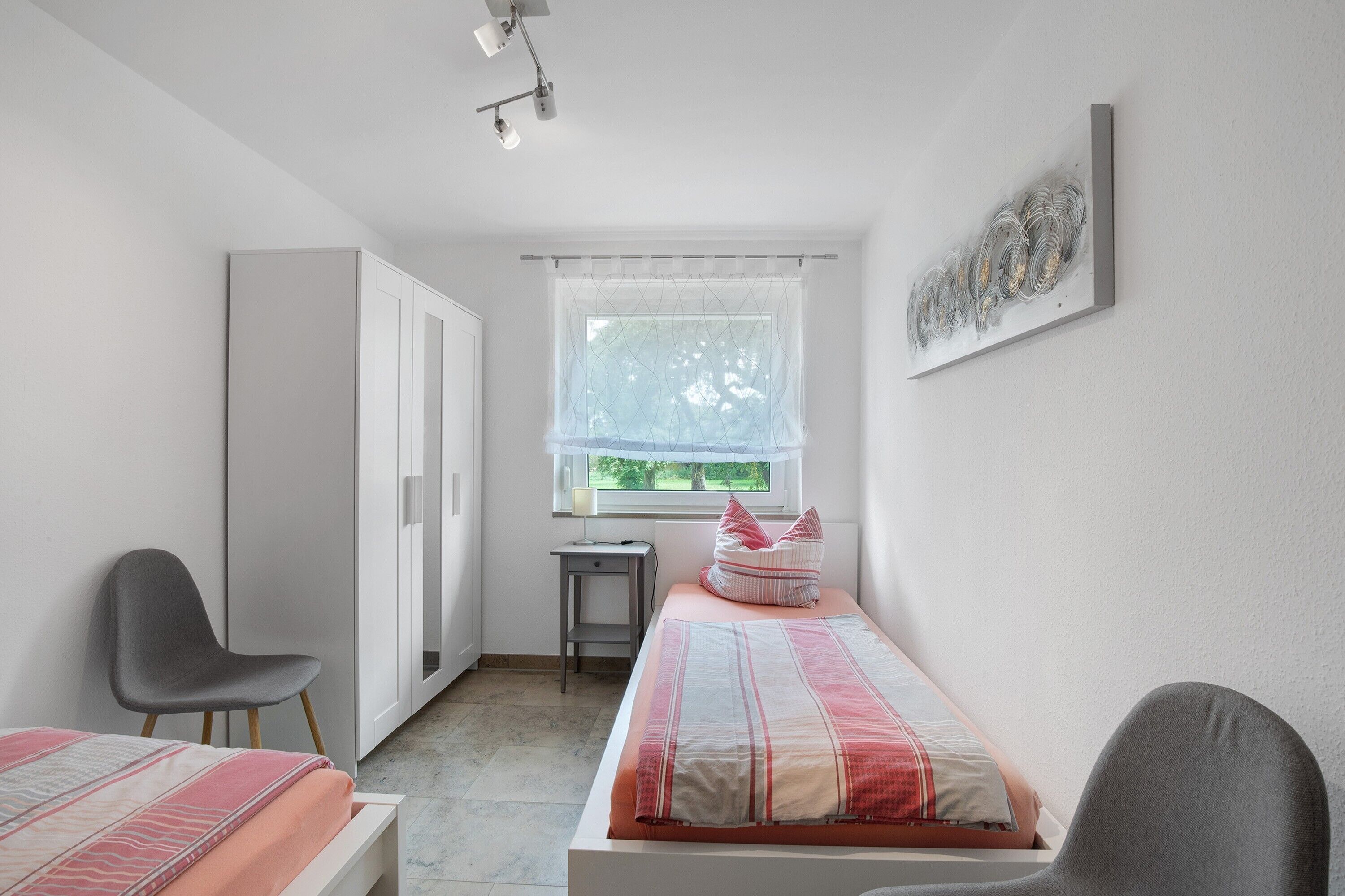 A bedroom with two single beds, a desk, a chair, and a wardrobe.