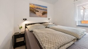 A bedroom with a bed, a nightstand with a vase, a wall-mounted picture, and a window with a view. - Holiday Home 'Zum Stumpfen Turm' with Sauna, Private Terrace and Garden (Morbach)