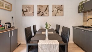 A dining area with a table set for four, surrounded by dark chairs, a vase with flowers, and framed artwork on the wall. - Holiday Home 'Zum Stumpfen Turm' with Sauna, Private Terrace and Garden (Morbach)
