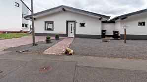 A building with a white facade, a grey roof, and a small entrance. There are two trash bins and a sign indicating the building's name. - Holiday Home 'Zum Stumpfen Turm' with Sauna, Private Terrace and Garden (Morbach)