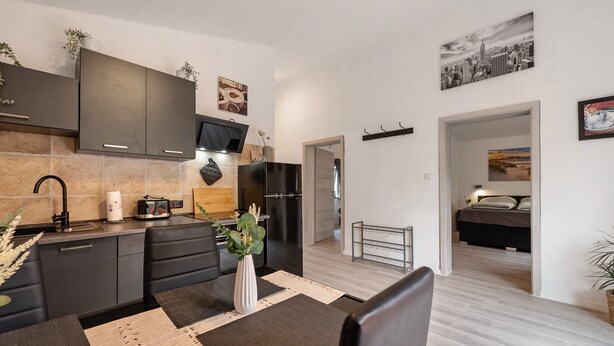 A modern kitchen with dark cabinets, a built-in oven, and a dining area with a table and chairs. - Holiday Home 'Zum Stumpfen Turm' with Sauna, Private Terrace and Garden (Morbach)