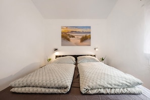 A bedroom with a bed, a wall-mounted picture, and a small plant.