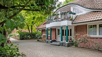 Een huis met een bakstenen gevel, een balkon met bloempotten en een verharde oprit.