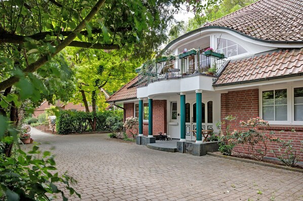 A house with a brick facade, a balcony with potted plants, and a paved driveway.