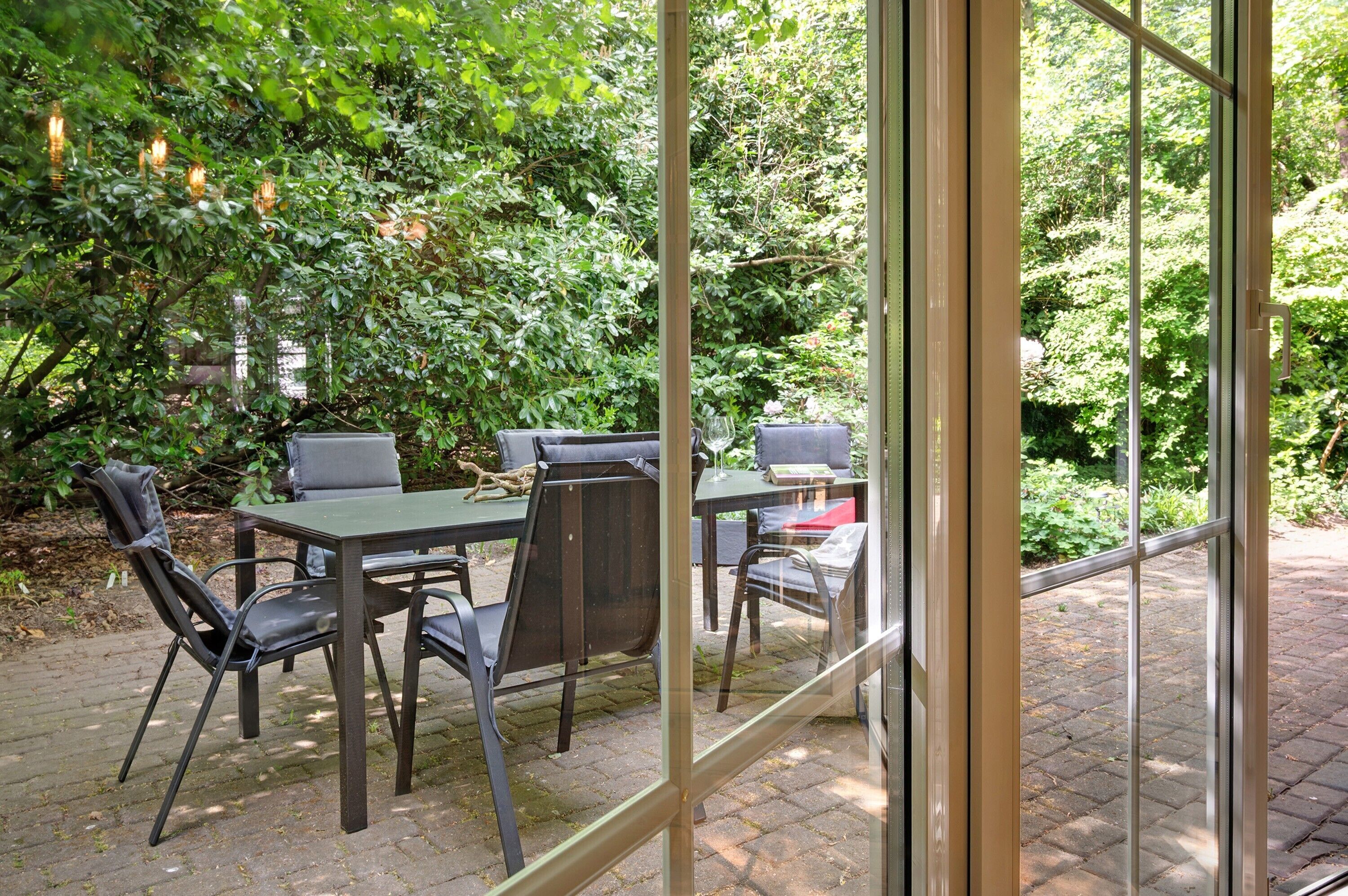 Een terras buiten met een tafel en stoelen, omgeven door weelderige beplanting.