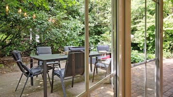 Een terras buiten met een tafel en stoelen, omgeven door weelderige beplanting.