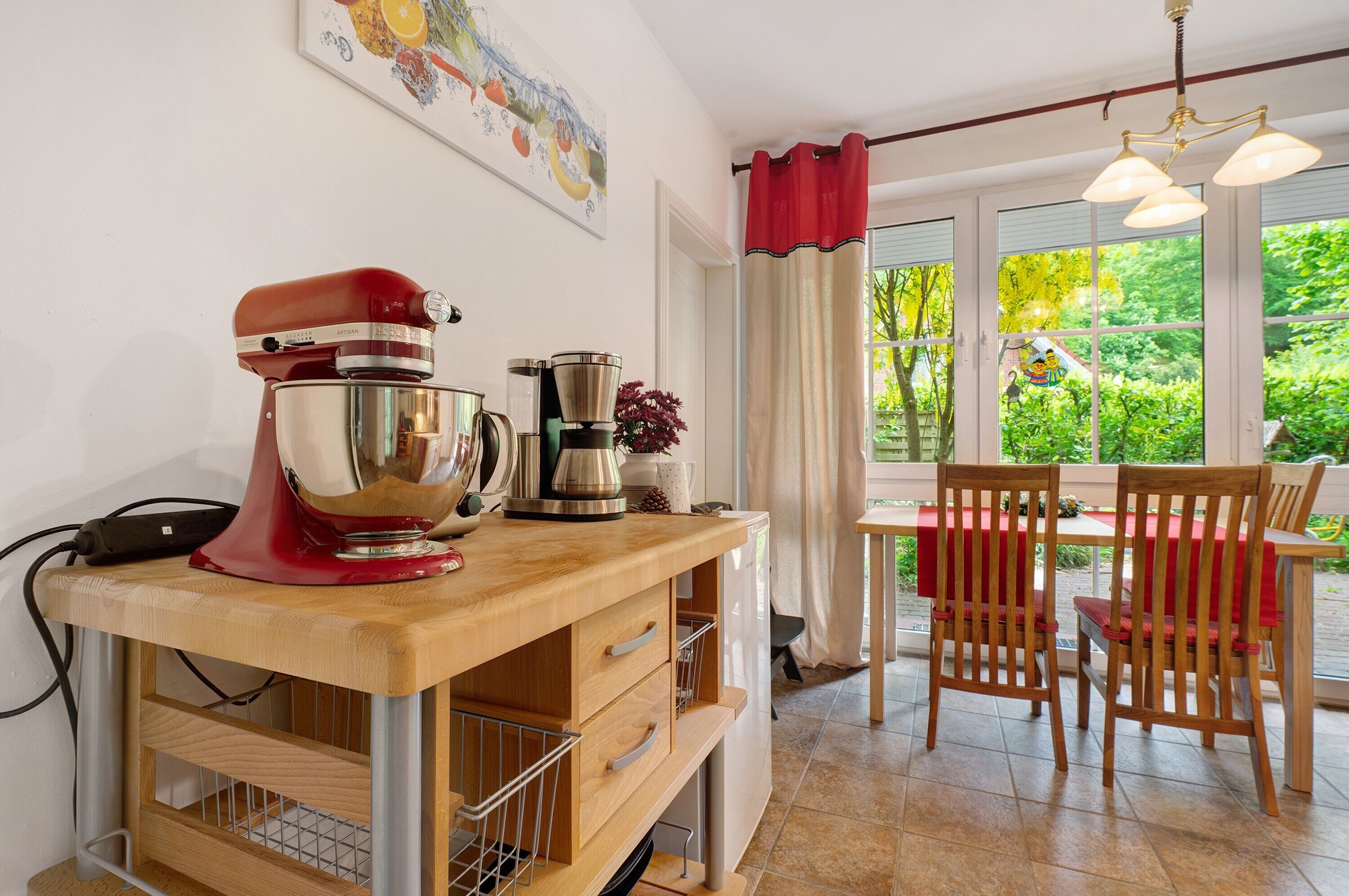 A kitchen with a mixer, a coffee maker, and a dining area with chairs and a table.