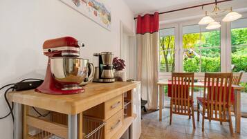 A kitchen with a mixer, a coffee maker, and a dining area with chairs and a table.