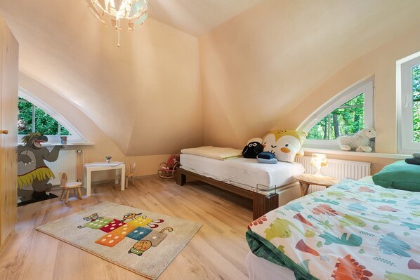 A child's bedroom with a loft bed, a small desk, and a window with a view of trees.