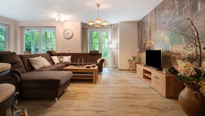 A living room with a sofa, coffee table, TV, and a painting. - Holiday Home 'Im Grünen' with Private Terrace, Private Garden and Wi-Fi (Harsefeld)