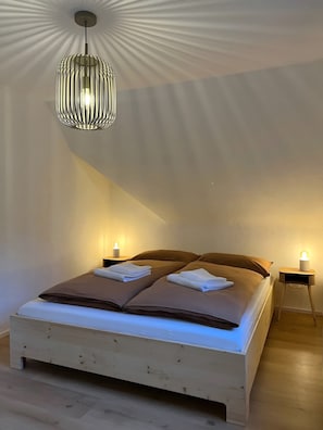 A bedroom with a bed, two bedside tables, a hanging light fixture, and a wall with a textured pattern. - Holiday Home Schmuckstück – Historic Old Town Retreat (Schiltach)