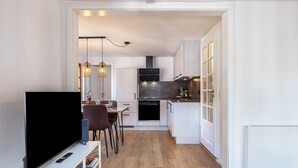 A modern kitchen with white cabinets, a built-in oven, and a dining area with a TV and seating.