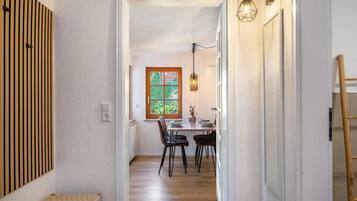 Un corridoio che conduce a una sala da pranzo con una panca di legno, un tavolo apparecchiato per due e una finestra con vista sul verde.