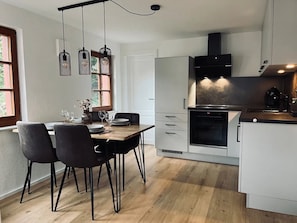 A modern kitchen with a dining area, featuring a wooden table, black chairs, and pendant lights. - Holiday Home Schmuckstück – Historic Old Town Retreat (Schiltach)