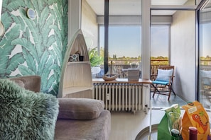 Un salon moderne avec vue sur la ville, un canapé confortable, une table d’appoint en bois et un fauteuil avec un coussin.