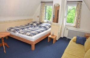Ein Schlafzimmer mit einem Bett, einem kleinen Tisch, einer Couch und zwei mit Vorhängen versehenen Fenstern.
