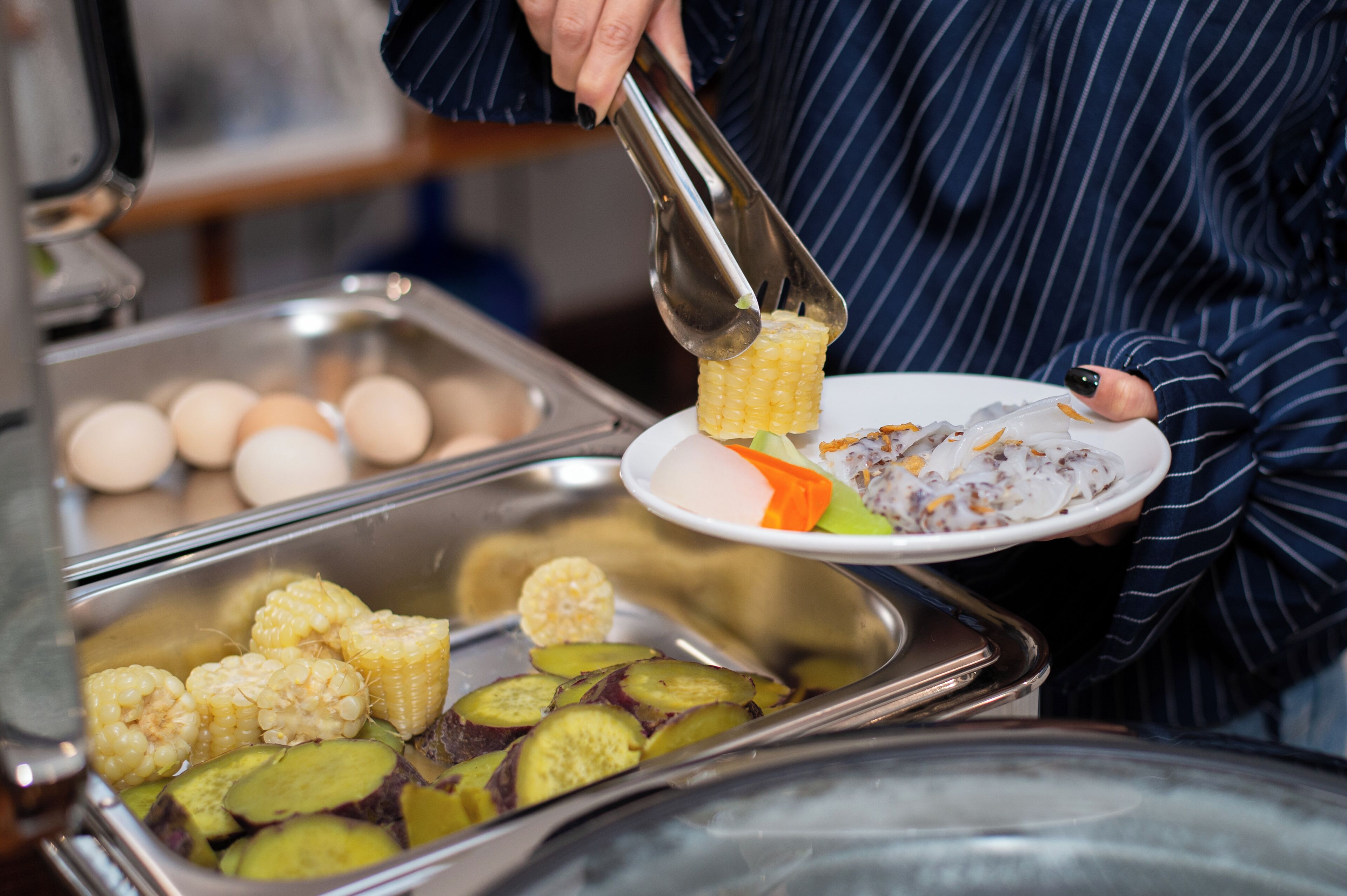 A buffet setup with various food items including corn, eggs, and vegetables.